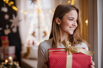 Happy young woman indoors at home at Christmas, holding present.