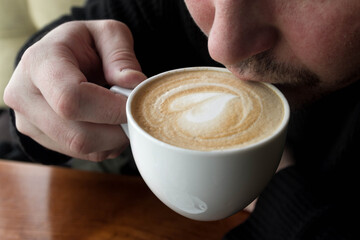 A man tries delicious coffee in a cafe. Heart in a coffee Cup.