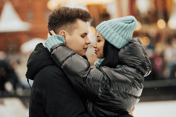 Fototapeta premium Close up portrait of young beautiful happy smiling couple. They hugging and looking at each other. Winter holidays, dating concept. Day light, snowfall.