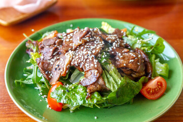 Green plate with lettuce and tongue, cherry tomatoes, sesame seed.