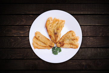 Three fried bananas on a top view white plate with a dark wood back screen.
