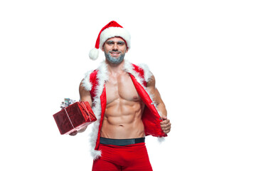 Sexy Santa Claus. Bodybuilder young handsome santa clause smile holds a gift in a red box and shows off abs cubes at New Years eve and Christmas winter holiday white background.