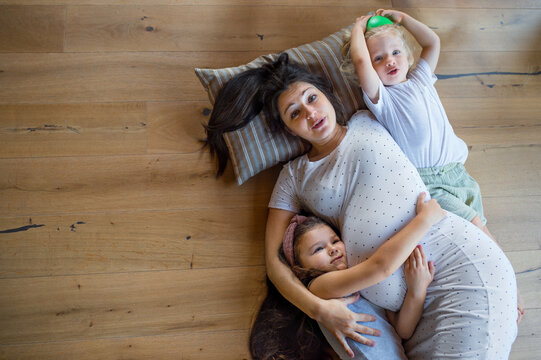 Top view of pregnant woman with small children indoors at home, lying on floor.