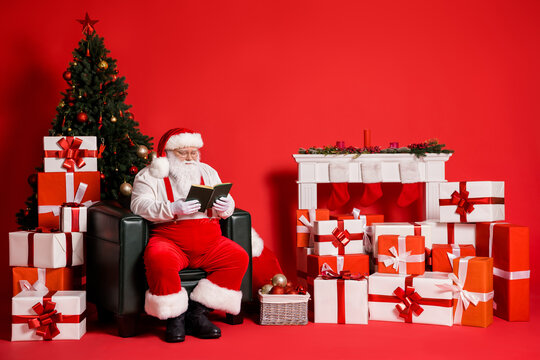 Portrait of his he attractive fat overweight focused concentrated wise Santa father sitting in armchair reading book spending festal day isolated bright vivid shine vibrant red color background