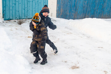 Two little European boys play and fight in the snow in winter.