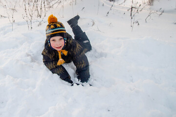 Fototapeta na wymiar A European boy lies in the snow in winter.