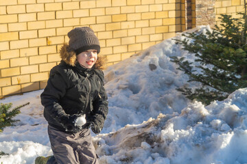 An active cheerful boy makes a lump of snow. Warm weather in winter.