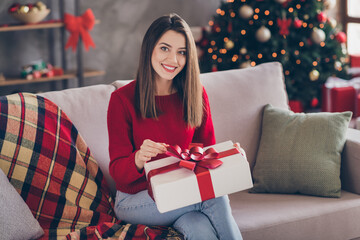 Photo of positive girl sit couch open x-mas gift box pull ribbon in house indoors with newyear...
