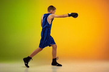 Fighter. Teenage professional boxer training in action, motion isolated on gradient background in neon light. Kicking, boxing. Concept of sport, movement, energy and dynamic, healthy lifestyle.