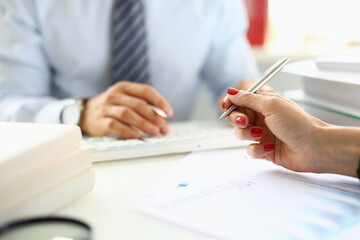 Female hand holds ballpoint pen over documents closeup in front of man in background in office. Conclusion business meeting concept.