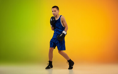 Champion. Teenage professional boxer training in action, motion isolated on gradient background in neon light. Kicking, boxing. Concept of sport, movement, energy and dynamic, healthy lifestyle.
