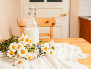 Obraz na płótnie Canvas Simply stylish wooden kitchen with bottle of milk and glass on table, summer flowers camomile, healthy foog moring concept