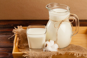 Pitcher of fresh milk on wooden table against beige background