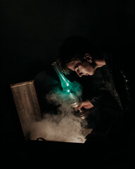 Young man in black leather jacket with a blue lamp looking into a open chest with smoke coming from...