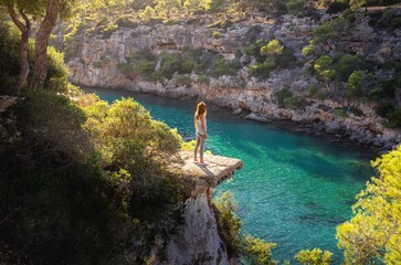 Girl standing on a ledge over the sea in beautiful soft sunlight, Cala Pi, Mallorca, Spain