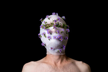 a portrait of a guy his head is wrapped in a bandage, flowers stick out of the bandage