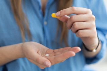 Close-up of woman's hands holding yellow medical pill against blue shirt.  Coronavirus disease outbreak.