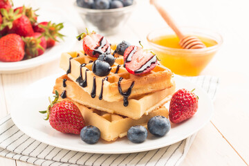 Fresh homemade food of berry Belgian waffles with honey, chocolate, strawberry, blueberry, maple syrup and cream. Healthy dessert breakfast concept with juice