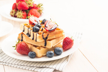 Fresh homemade food of berry Belgian waffles with honey, chocolate, strawberry, blueberry, maple syrup and cream. Healthy dessert breakfast concept with juice