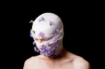 a portrait of a guy his head is wrapped in a bandage, flowers stick out of the bandage
