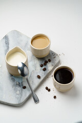 Coffee and milk in ceramic cups with beans, marble