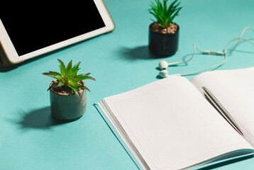 A workplace with a notebook, headphones, earphones, laptop, pen, and succulents in pods. Working place for a freelancer on a light blue background. Working from home concept. Side view, copy space