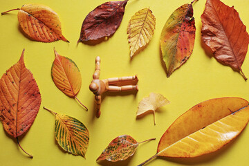 黄色い紙の上に置いた複数の落ち葉と木製の人形。秋のイメージ。