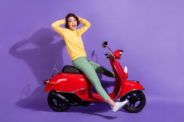 Fototapeta na wymiar Full length body size side profile photo of female student with brunette bob hair driving red motorbike smiling keeping hands on head isolated on bright purple color background