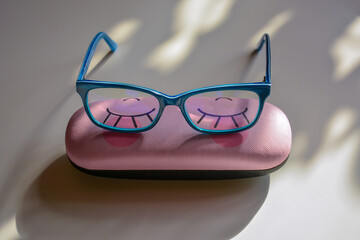 Rectangular glasses in bright blue frames on a funny case for glasses light background close-up
