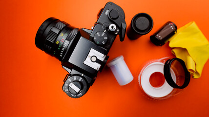 Old camera from the analogue era on an orange background and with film reels and goblets around