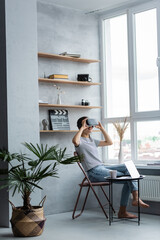 Barefoot freelancer using vr headset near laptop and cup on coffee table at home