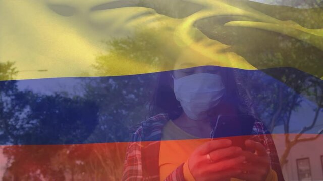 Colombian flag waving against woman wearing face mask using smartphone