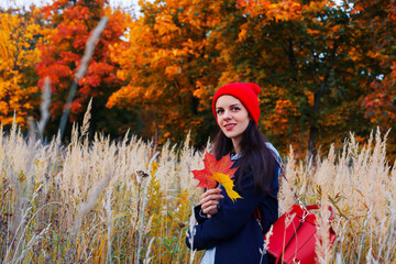 Woman with long hair and attractive smile standing in autumn field with colorful forest on background.