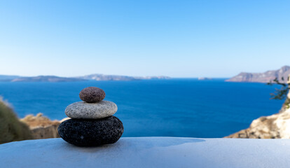 Close-up shot of pebbles stacked on each other in a balance with santorini caldera in the background