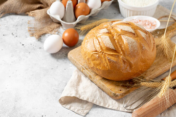 Wheat round bread. Wheat bread is surrounded by baking ingredients. Bread close-up. Eggs, salt, flour, seeds on the kitchen table