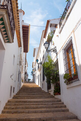 Beautiful narrow street in Altea, Costa Blanca, Valencian Community, Spain. Historical center/old town. Stone stairs going up. Vertical shot. Typical ancient architecture.