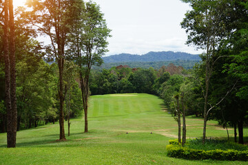 Fototapeta na wymiar Background of evening golf course has sunlight shining down at golf course in Thailand. Nice scenery on a golf course at a late summer afternoon