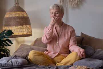 Senior woman practicing yoga at home, making Alternate Nostril Breathing exercise, nadi shodhana...