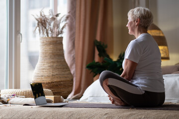 Middle age caucasian sportswoman sitting on mat with smile on face using laptop at home