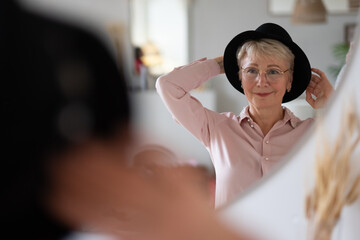 Caucasian woman trying on hat looking in mirror at home preparing for walk.