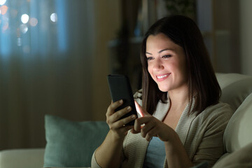 Happy woman using cell phone in the night at home