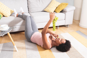 Happy woman eating grapes lying down on carpet at home