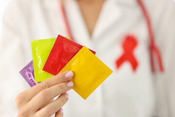 Infectious disease doctor with red ribbon on uniform holds lot of condoms in hand closeup....