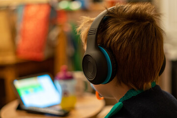 A small child wearing headphones watching a tablet with a blurred background