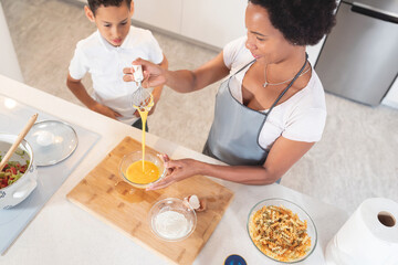 Boy looking at mother whisking egg in the kitchen