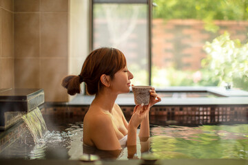Young woman relaxing in hot spring and drinking tea