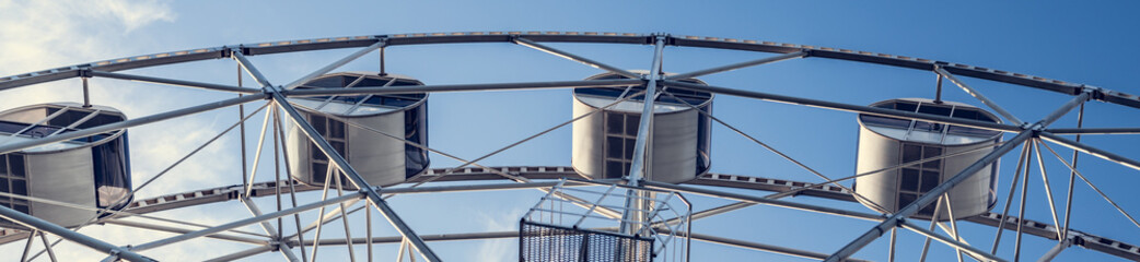 Gray or white metal ferris wheel with closed passenger cabins close-up in the amusement park