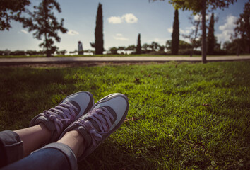 Piernas de mujer vistiendo jeans y zapatillas clásicas mientras yace sobre el césped del parque...