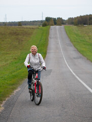 Portrait of woman riding bicycle on dirty road in countryside,cyclist on a way between fields,cyclist touring in Lithuania,by bicycle in countryside, happy woamn cycling bicycle .Travel concept