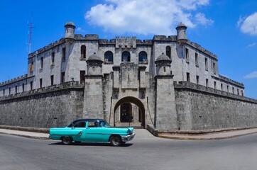 Turquoise colored american classic car in front of an old fortress in Havana, Cuba, blue sky with clouds, a sunny day in summer